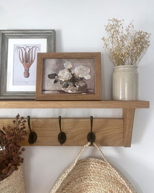 a wooden shelf with hooks and flowers on it next to a hat hanging from the wall