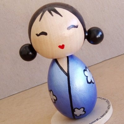 a wooden figurine with black hair and blue dress sitting on top of a table