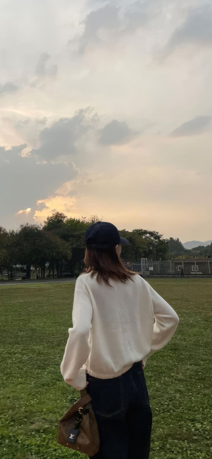 a woman standing on top of a lush green field holding a brown bag in her hand