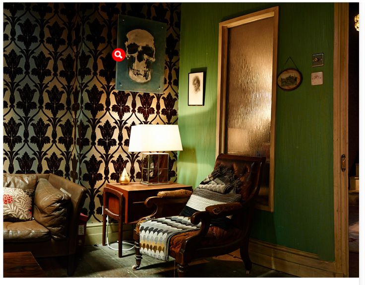 a living room with green walls and patterned wallpaper, two leather chairs and a small table