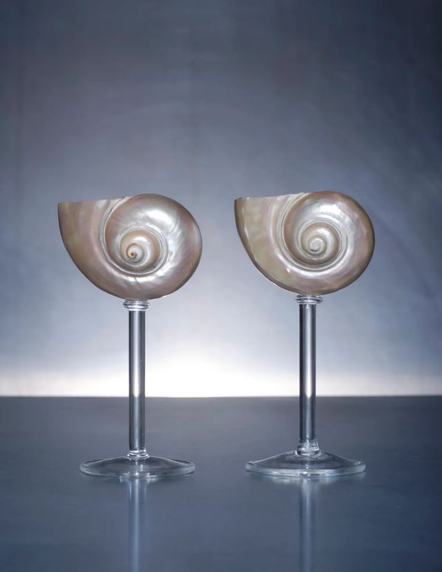 two wine goblets sitting on top of each other in front of a gray background