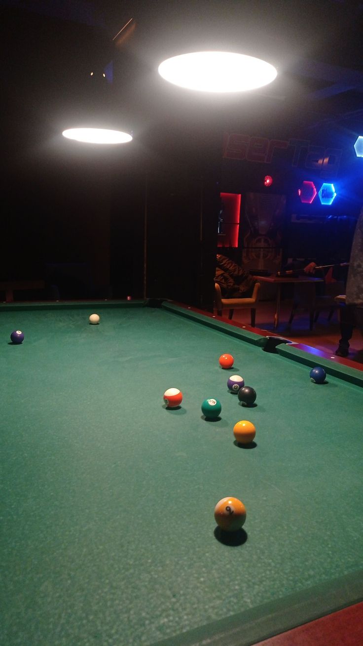 a pool table with several balls on it in a room lit up by blue lights