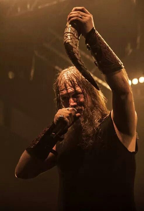 a man with long hair holding a microphone up to his head while standing in front of a crowd