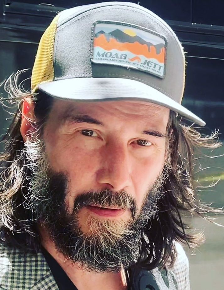 a man with long hair and a beard wearing a hat is looking at the camera