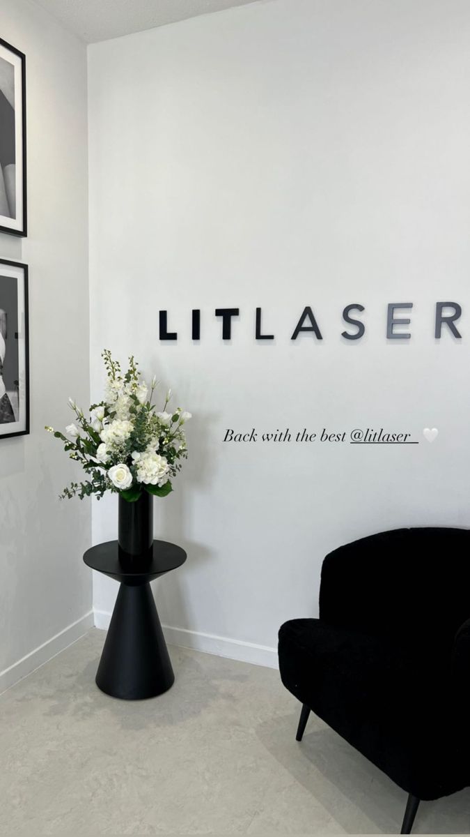 a black chair sitting next to a vase with flowers on it in front of a white wall