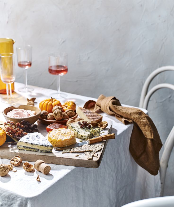 an assortment of cheeses, nuts and other foods on a table with wine glasses