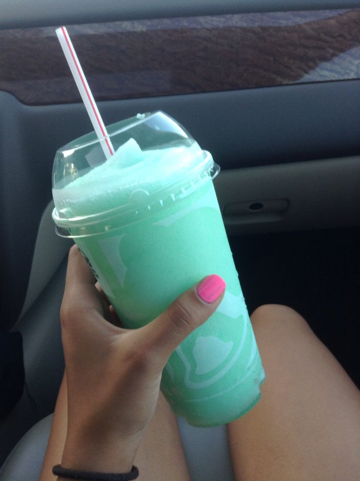 a woman holding a green drink in her hand while sitting in the backseat of a car