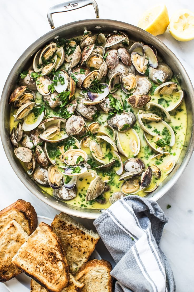 a pan filled with clams and bread on top of a white counter next to lemon wedges