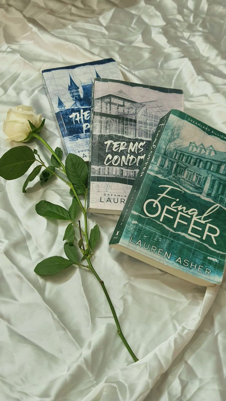 three books are laying on a bed with a rose in front of them and the cover is white