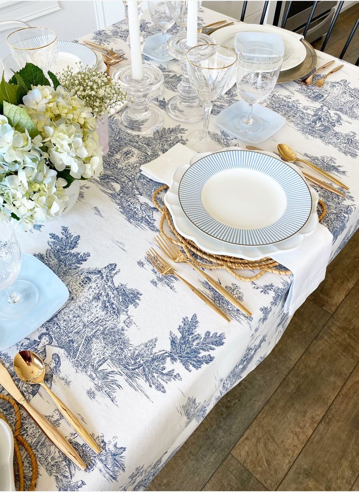 a table set with blue and white plates, silverware and flowers in vases