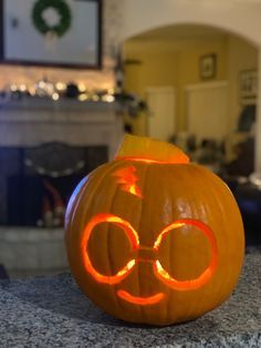 a pumpkin with glasses carved into it's face on a table in front of a fireplace