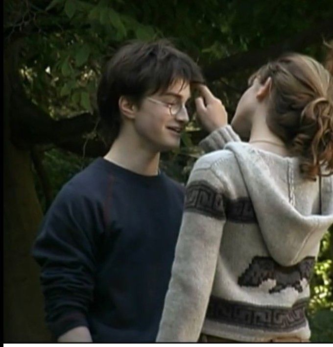 two people standing next to each other in front of trees and one person wearing glasses