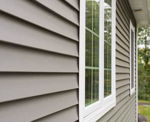 the side of a gray house with white windows