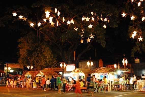 many people are standing around in the street at night with stars hanging from the trees