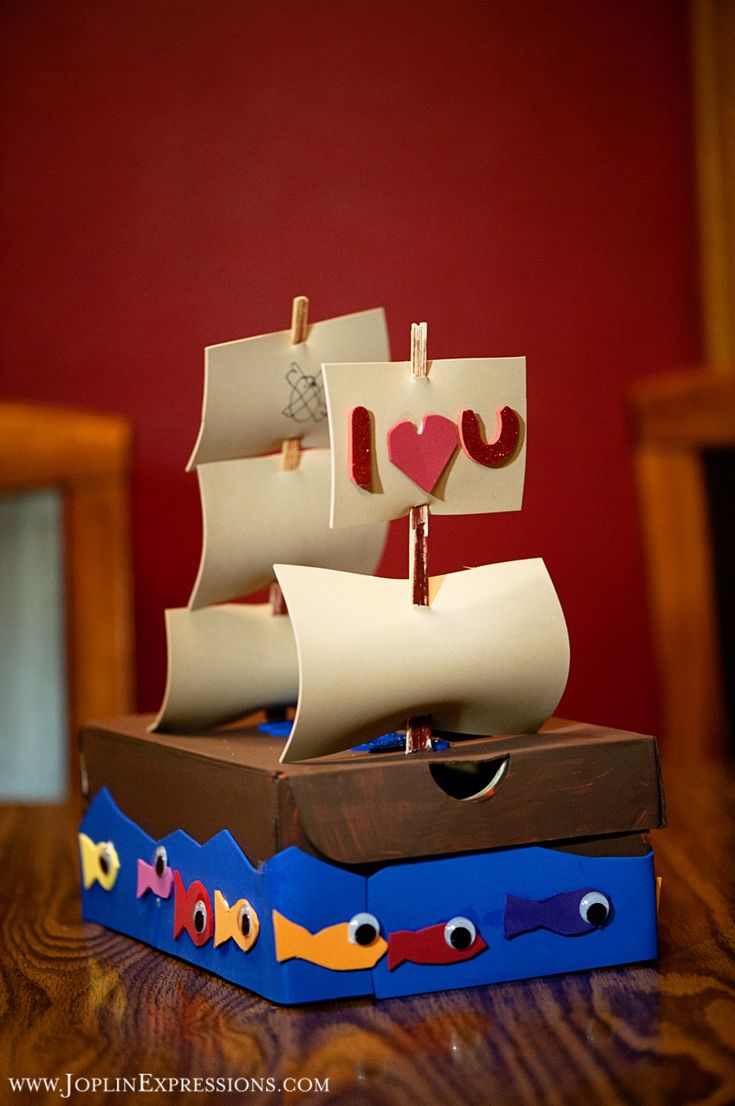 a paper boat with hearts on it is sitting on a wooden table in front of a red wall