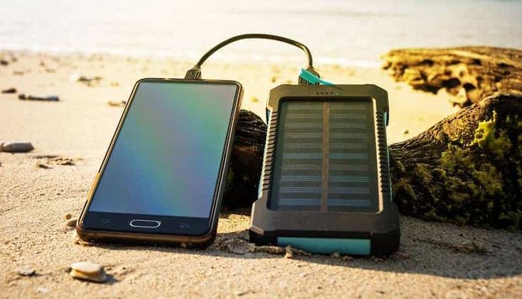 an open cell phone sitting on top of a sandy beach next to a charging device