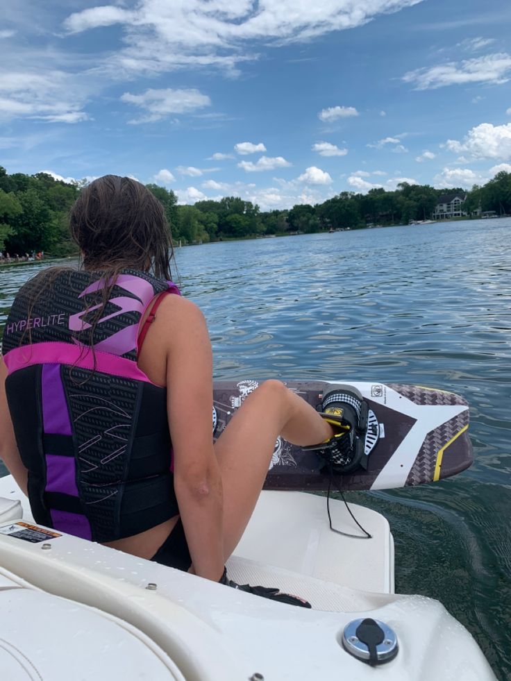 a woman riding on the back of a boat with a wake board in her hand