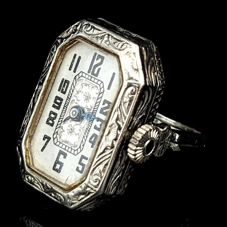 Presenting a remarkable Art Deco era ring watch convertible to wrist watch, a true novelty piece that encapsulates the elegance and ingenuity of the past. Crafted in 14k white gold, this antique/vintage piece features a double shank that cleverly opens up into watch lugs, allowing for the watch to be converted into a wrist watch with the addition of a cord strap (not included). The white dial adorned with Arabic numerals and beautiful floral accents sits within an exquisitely engraved case, a te Luxury Art Deco Watch With Manual Winding, Antique Platinum Evening Watches, Antique Rectangular Evening Watch, Timeless Engraved Evening Watches, Antique Platinum Jewelry And Watches For Evening, Timeless Self-winding Evening Watch, Antique Formal Watch Accessories With Polished Finish, Antique Watch Accessories With Polished Finish For Formal Occasions, Timeless Rectangular Dial Jewelry For Evening