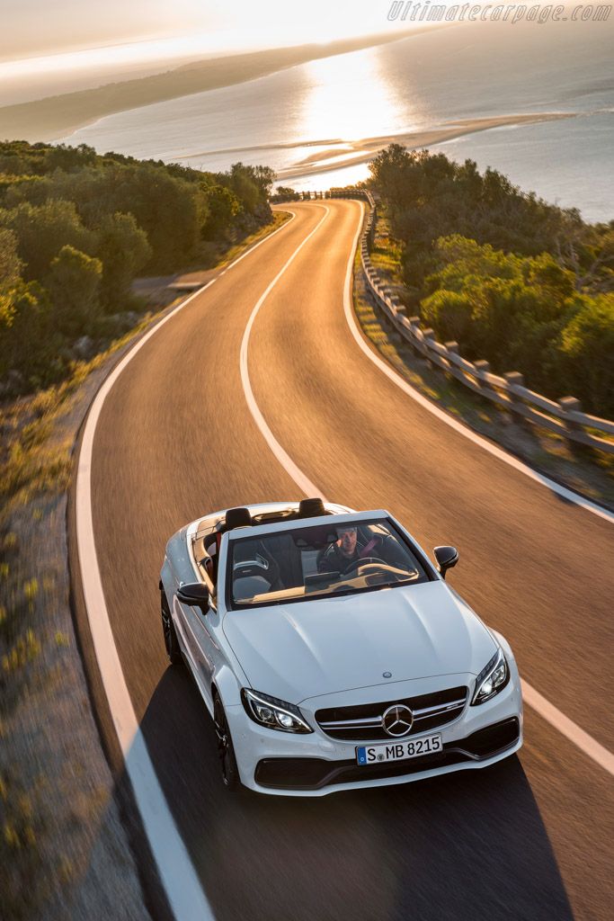 a white car driving down a road next to the ocean