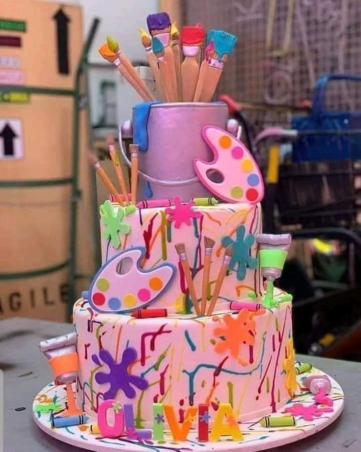 a multi - tiered birthday cake decorated with paint splatters and pencils