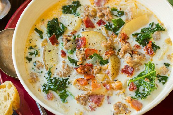 a bowl of soup with meat, spinach and cheese on the side next to bread