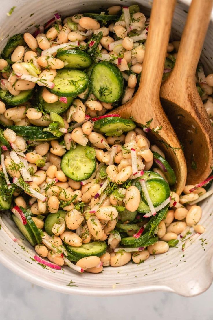 a bowl filled with beans, cucumbers and onions next to a wooden spoon