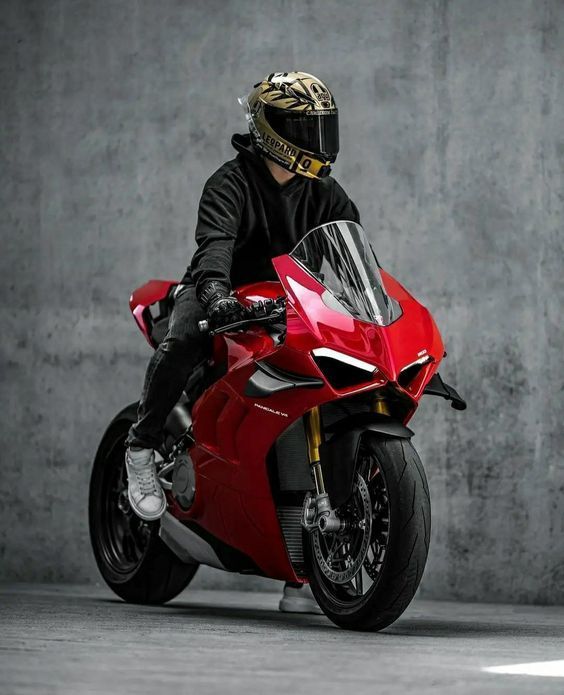 a man riding on the back of a red motorcycle in front of a cement wall