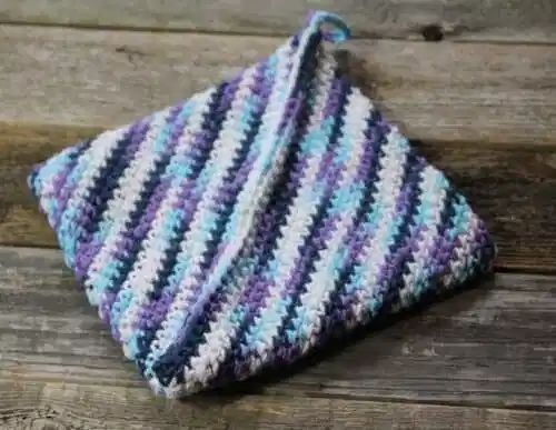 a crocheted dish cloth sitting on top of a wooden table next to a piece of wood