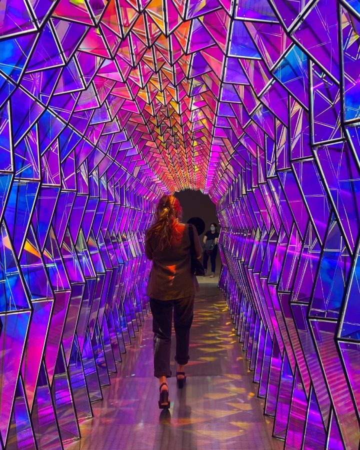 a woman walking down a long tunnel covered in colorful lights