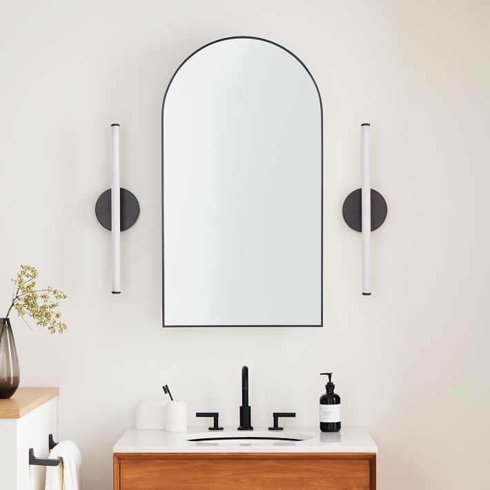 a bathroom with a sink, mirror and two black faucets on the wall