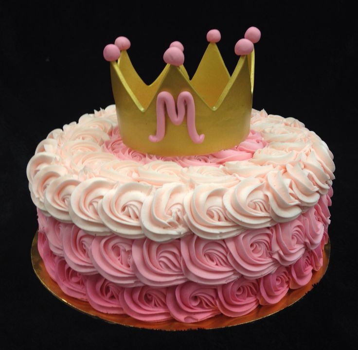 a cake with pink frosting and a gold crown on top, sitting on a black surface