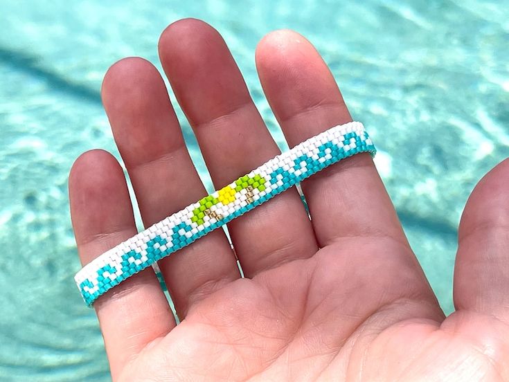 a hand holding a small bracelet in front of a pool with blue and green water