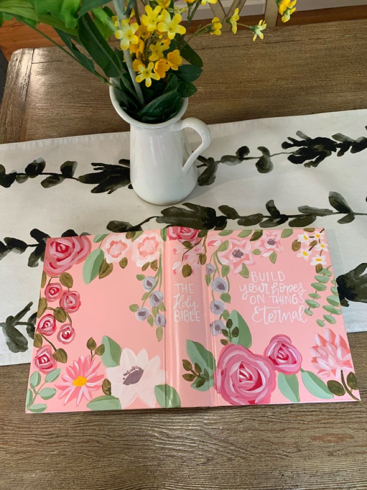 an open book sitting on top of a table next to a vase filled with flowers