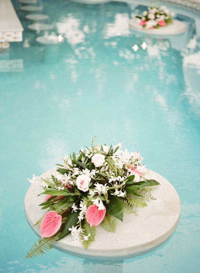 flowers and greenery are placed on the edge of a swimming pool in an outdoor setting