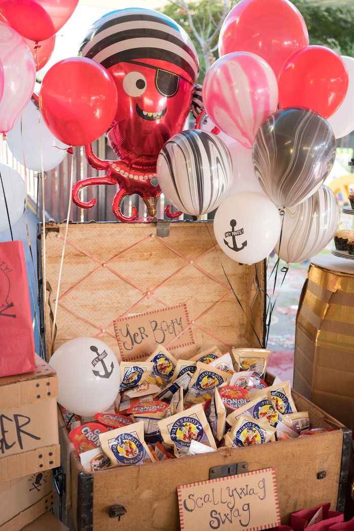 a trunk filled with candy and balloons on top of a wooden table next to other items