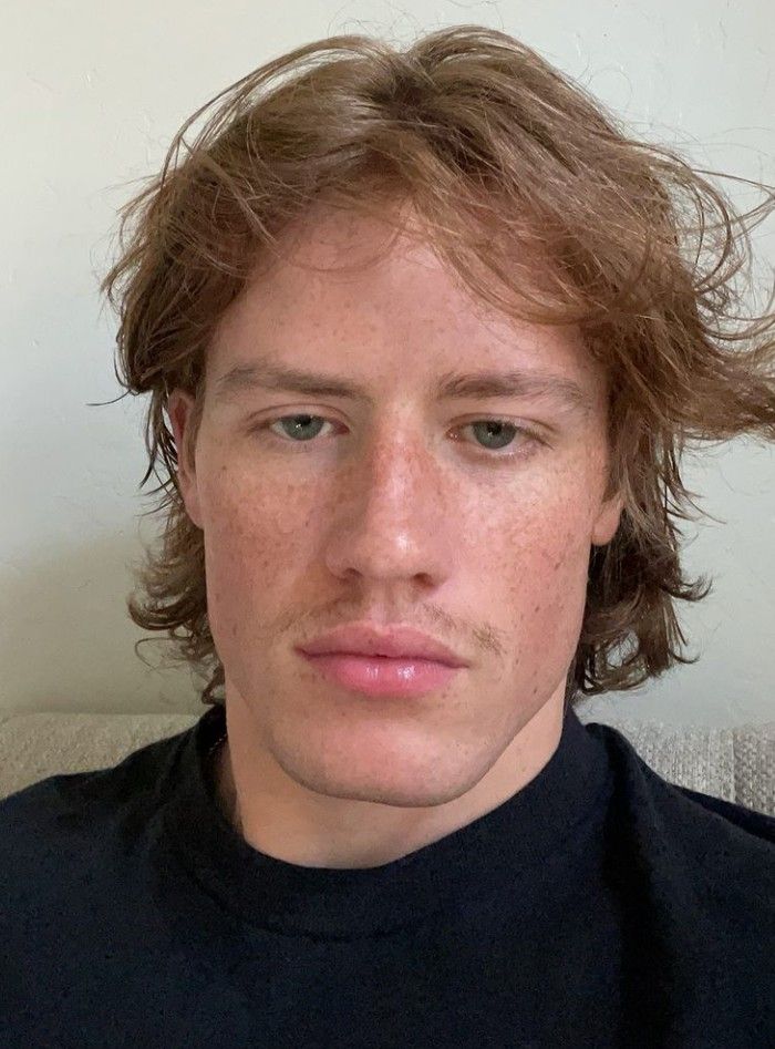 a young man with freckled hair looks at the camera while wearing a black shirt