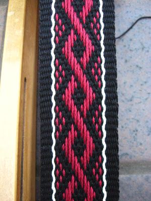 a red and black knitted tie sitting on top of a wooden chair next to a wall