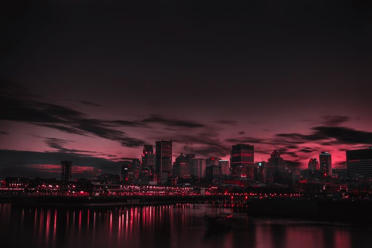 the city is lit up at night with red lights in the sky and reflecting on the water