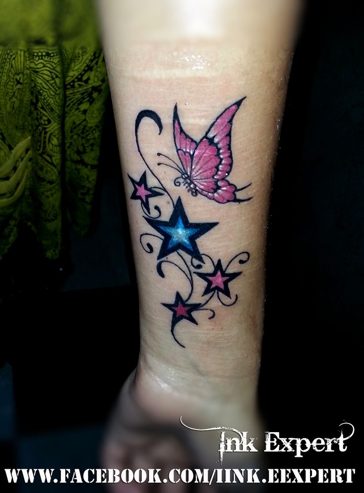 a small butterfly tattoo on the wrist with stars and swirls around it's wings