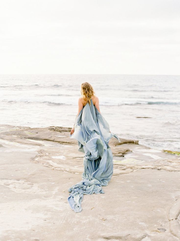 a woman in a blue dress walking on the beach with her back to the camera