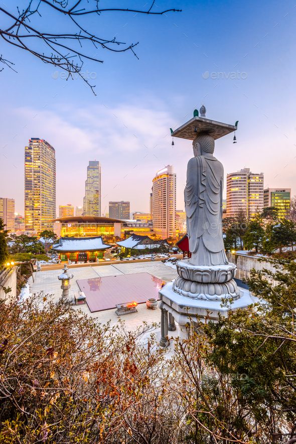 a statue in the middle of a park with tall buildings in the background