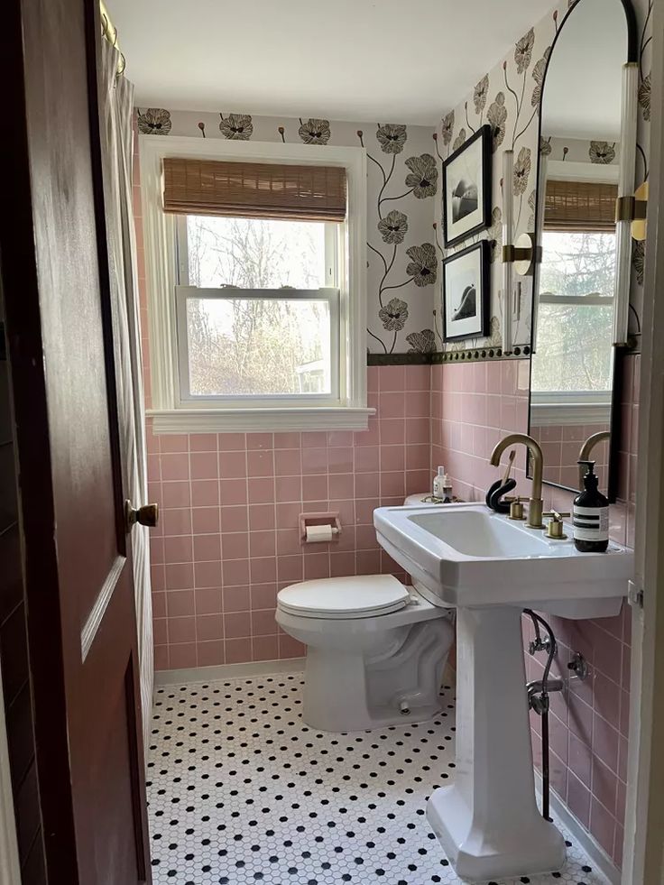 a bathroom with pink and black tiles on the floor, sink, toilet and mirror