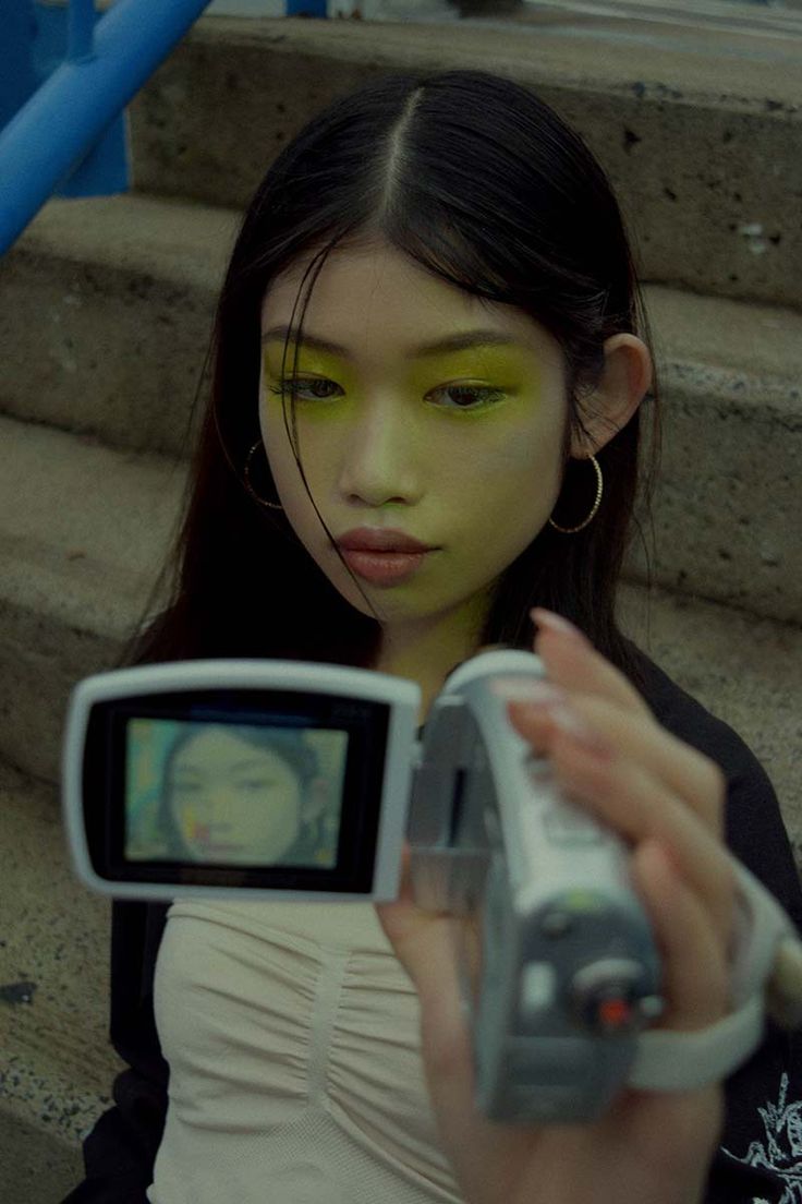 a woman holding a camera up to her face and looking at the camera with green eyes