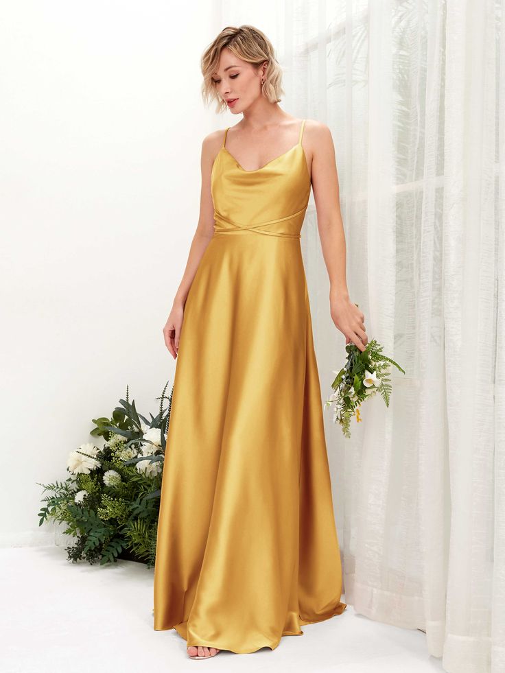 a woman in a gold dress standing next to a white curtain and holding a bouquet