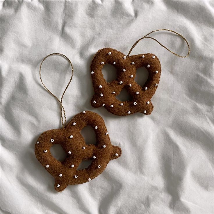 two ornaments made to look like pretzels hanging from strings on a white sheet