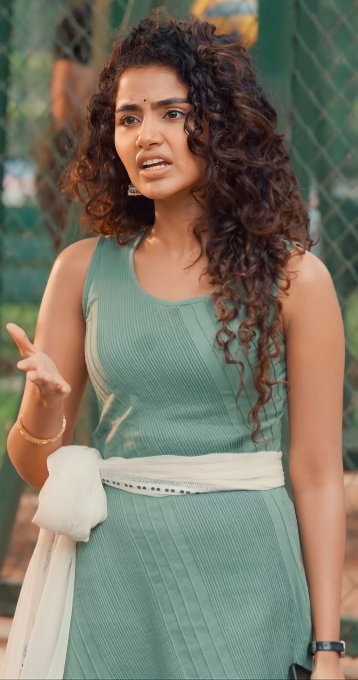 a woman with curly hair wearing a green dress and holding her hand out to the side