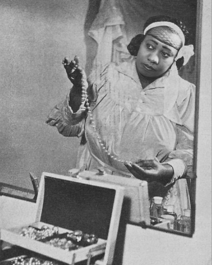 an old black and white photo of a woman holding something in her hand while standing next to jewelry boxes