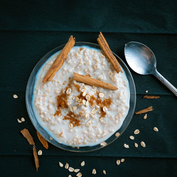 a bowl of oatmeal with cinnamon sticks and nuts on the side next to a spoon