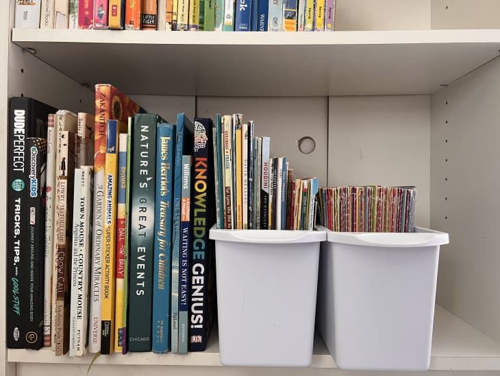 two white bins sitting on top of a book shelf filled with lots of books