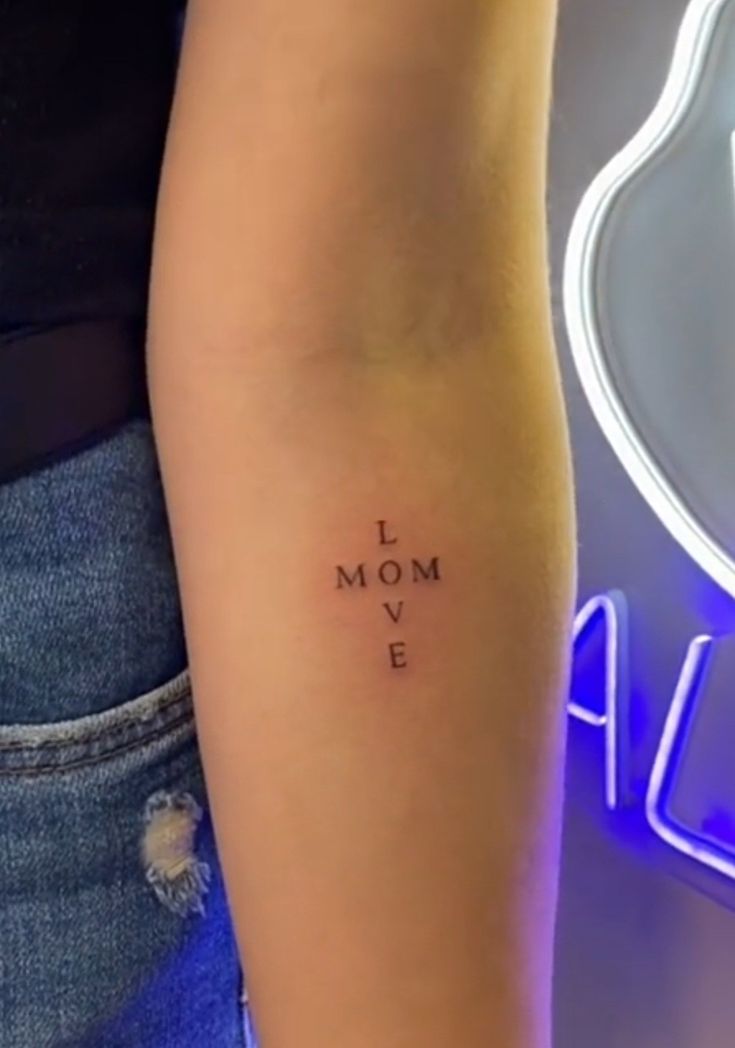 a woman with a tattoo on her arm that says i love mom e in cursive writing